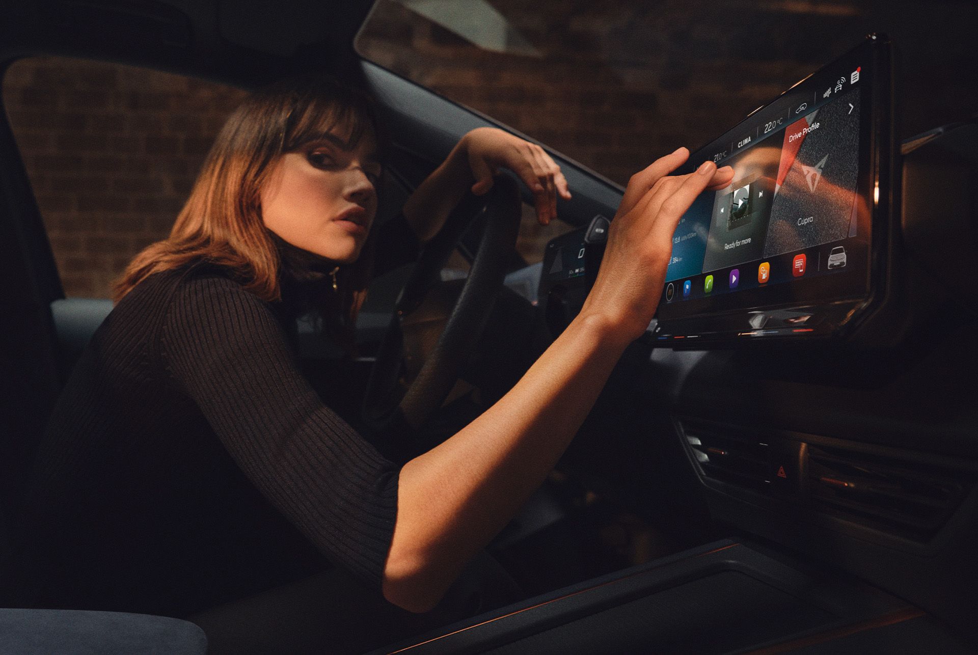 Eine Frau sitzt in einem CUPRA Born und bedient das Infotainment Display.