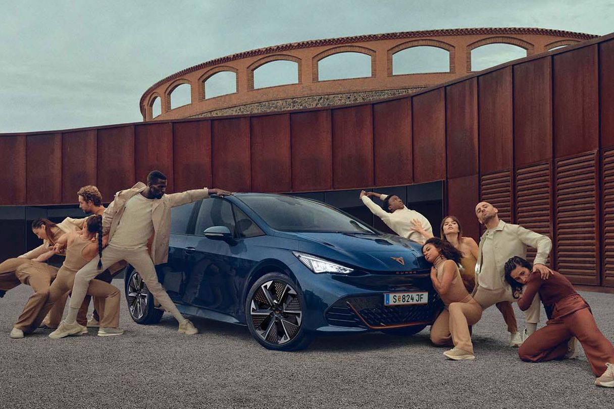 Ein blauer CUPRA Born steht auf einem Platz, mehrere Personen befinden sich links und rechts neben dem Fahrzeug.