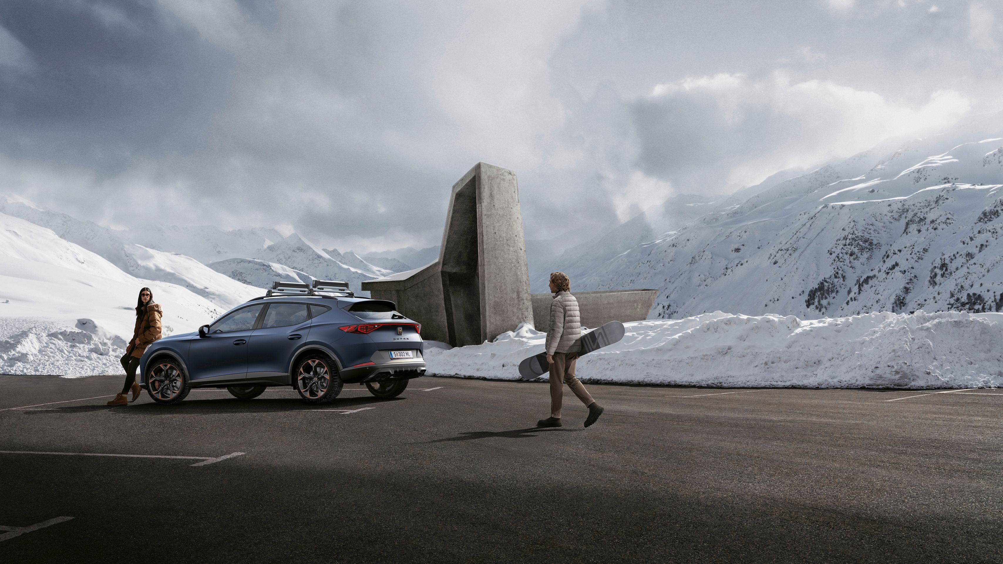Eine Frau lehnt an einem CUPRA Formentor auf einem winterlichen Parkplatz in den Bergen. Ein Mann mit Snowboard bewegt sich in Richtung des Fahrzeugs.