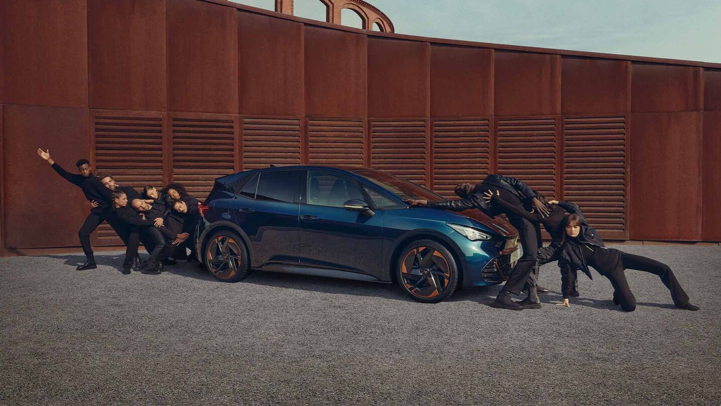 Ein blauer CUPRA Born steht auf einem Platz, Menschen performen neben dem Fahrzeug.