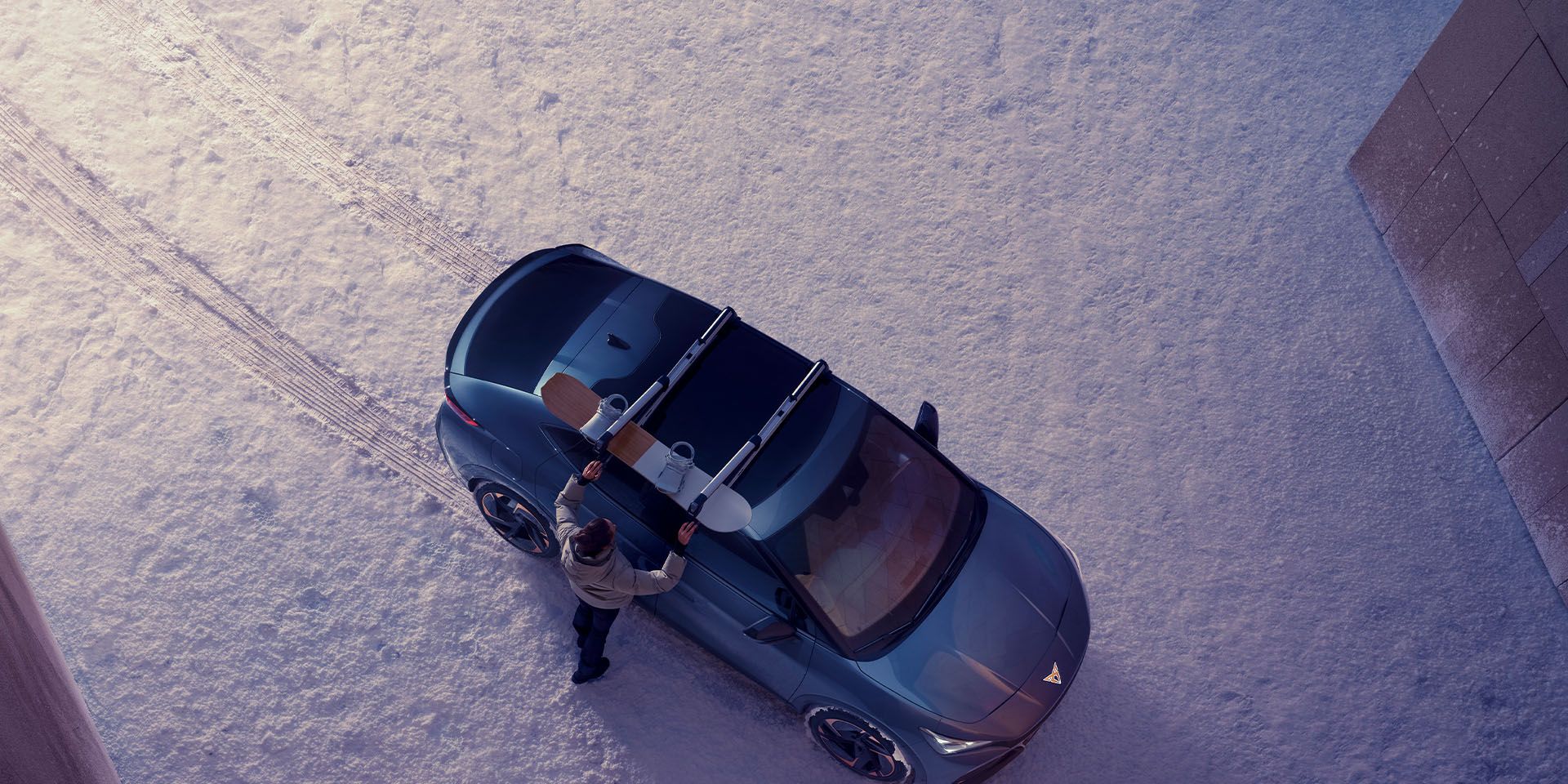 Eine Person befestigt ein Snowboard am Skiträger eines CUPRA Tavascan.