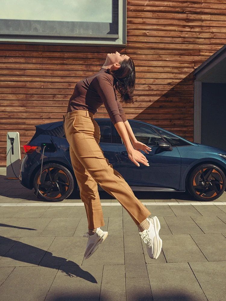 Eine Frau springt in die Luft, im HIntergrund ein CUPRA Born